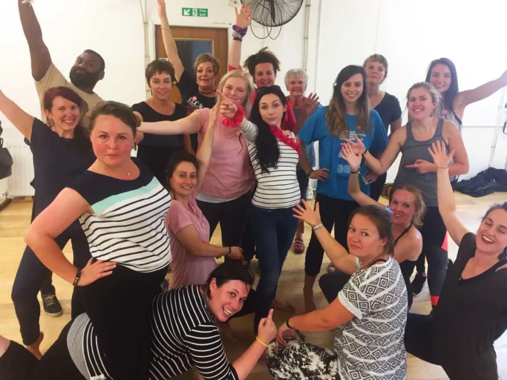 A group of friends laughing and posing with their arms in the air after a dance session in the studio