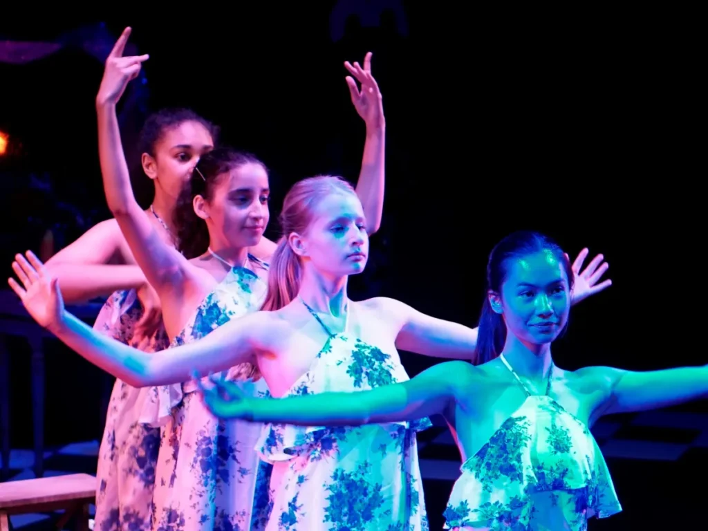 Teenage dancers in matching floral dresses performing on stage with their arms raised, at a Hype Dance show