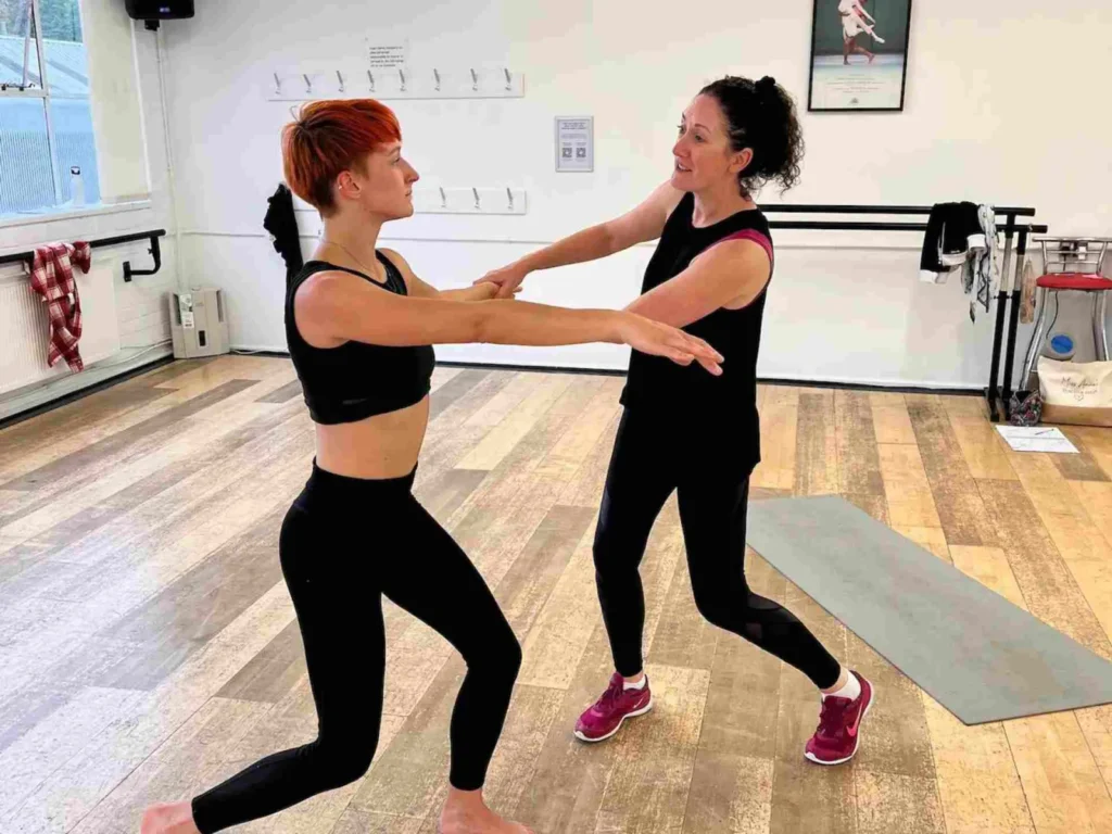 A teacher guiding a student by the arm as they lunge together in a private dance lesson at the studio